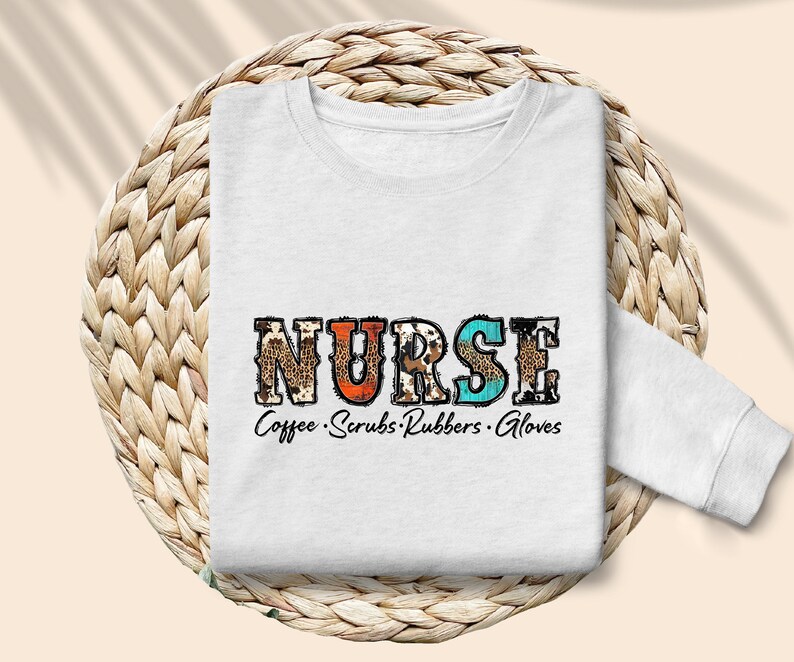 May include: White sweatshirt with the word "NURSE" in colorful patterned letters. The text "Coffee. Scrubs. Rubbers. Gloves" is printed below the word "NURSE".