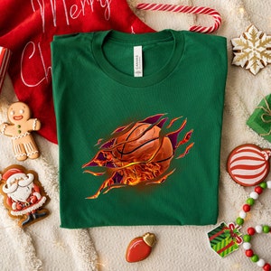 May include: Green t-shirt with a basketball bursting out of the fabric, surrounded by flames. The basketball is orange and brown with black lines.