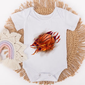 May include: White baby onesie with a graphic of a basketball bursting through the fabric with flames. The basketball is orange and brown.