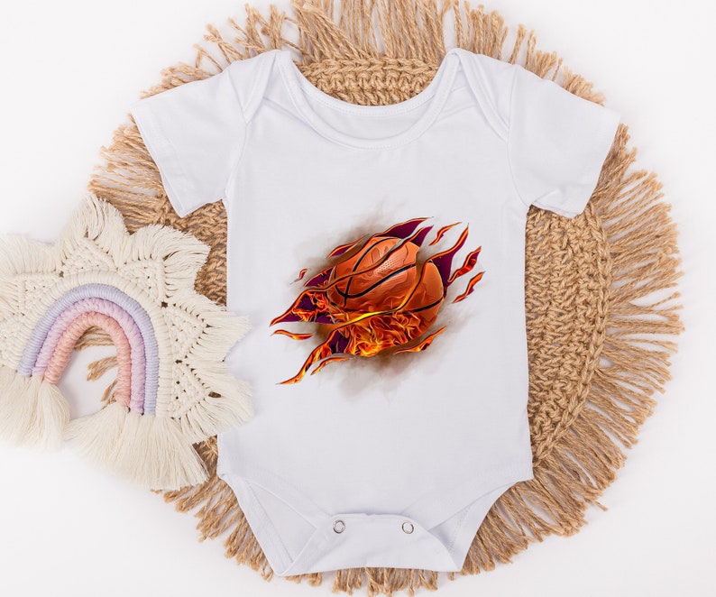 May include: White baby onesie with a graphic of a basketball bursting through the fabric with flames. The basketball is orange and brown.