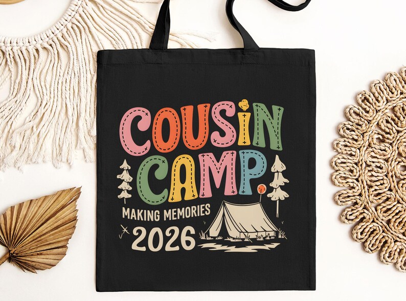 May include: Black tote bag with the words "COUSIN CAMP" in colorful, stitched-style letters. Below, it reads "MAKING MEMORIES 2026" with a tent graphic. The bag has black handles.