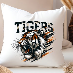 K&ouml;nnte beinhalten: Ein wei&szlig;es Kissen mit einem Motiv eines Tigerkopfes und dem Wort "TIGERS" in schwarzen Buchstaben. Der Tiger hat orange und schwarze Streifen auf wei&szlig;em Hintergrund. Das Motiv ist von schwarzen und orangefarbenen Streifen umgeben.