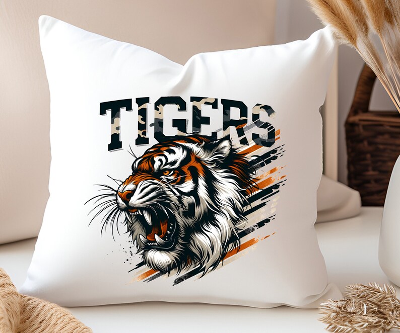 K&ouml;nnte beinhalten: Ein wei&szlig;es Kissen mit einem Motiv eines Tigerkopfes und dem Wort "TIGERS" in schwarzen Buchstaben. Der Tiger hat orange und schwarze Streifen auf wei&szlig;em Hintergrund. Das Motiv ist von schwarzen und orangefarbenen Streifen umgeben.