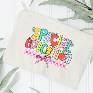 May include: A white canvas zippered pouch with a colorful graphic that says "Special Education" with a pink bow and a red apple.