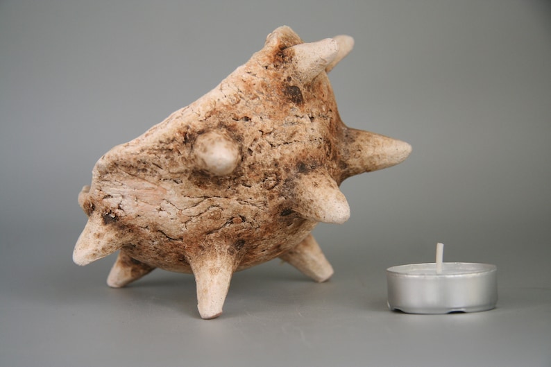 Puede incluir: Un portavelas de cer&aacute;mica con forma de criatura marina espinosa, de color marr&oacute;n y blanco. El portavelas tiene una peque&ntilde;a vela de t&eacute; plateada en su interior.