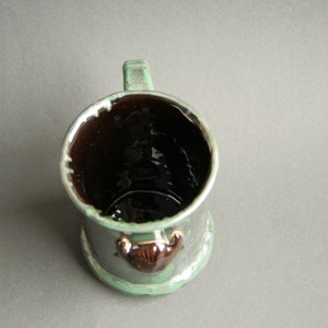 May include: A green ceramic mug with a brown interior and a brown animal figurine on the front.