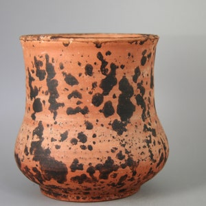 Pode incluir: Um vaso de terracota com um esmalte marrom e preto salpicado. O vaso tem uma base larga e um pescoço estreito.