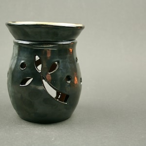 May include: Black ceramic oil burner with a leaf design. The burner has cutouts in the shape of leaves and circles.