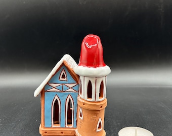 May include: A ceramic Christmas house candle holder with a blue and white exterior and a red roof. The house has a tower with a white trim and a red roof. A white tea light candle is included.