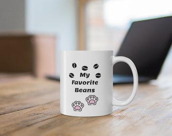 May include: White ceramic coffee mug with black text that reads "My Favorite Beans" and two pink paw prints.