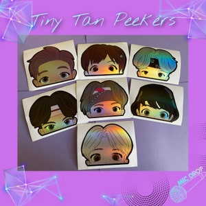 May include: Seven holographic stickers featuring cartoon faces peeking over a surface. The faces are of different genders and ethnicities, with various hairstyles and expressions. The stickers are labelled "Tiny Tan Peekers".