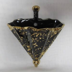 May include: Black and gold ceramic wall planter shaped like an umbrella. The planter has a speckled gold design and a gold rim.