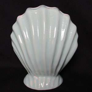 May include: A light blue ceramic vase shaped like a seashell. The vase has a smooth, glossy finish and a wide opening at the top.