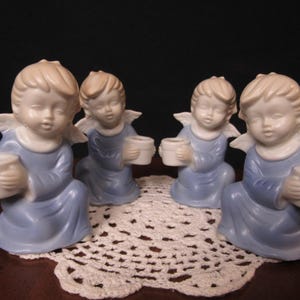 May include: Set of four blue and white porcelain angel candle holders. Each angel is holding a small white cup for a candle.