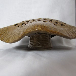 May include: A ceramic mushroom-shaped planter with a brown glaze and a lattice design on the top. The planter has a wide, flat base.