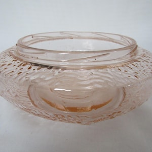 May include: A vintage, light pink glass bowl with a textured exterior. The bowl has a wide, rounded shape with a slightly flared rim. The textured surface has a wave-like pattern. The bowl is likely used for decorative purposes.