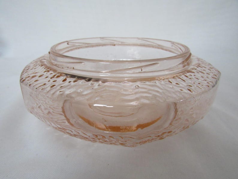 May include: A vintage, light pink glass bowl with a textured exterior. The bowl has a wide, rounded shape with a slightly flared rim. The textured surface has a wave-like pattern. The bowl is likely used for decorative purposes.