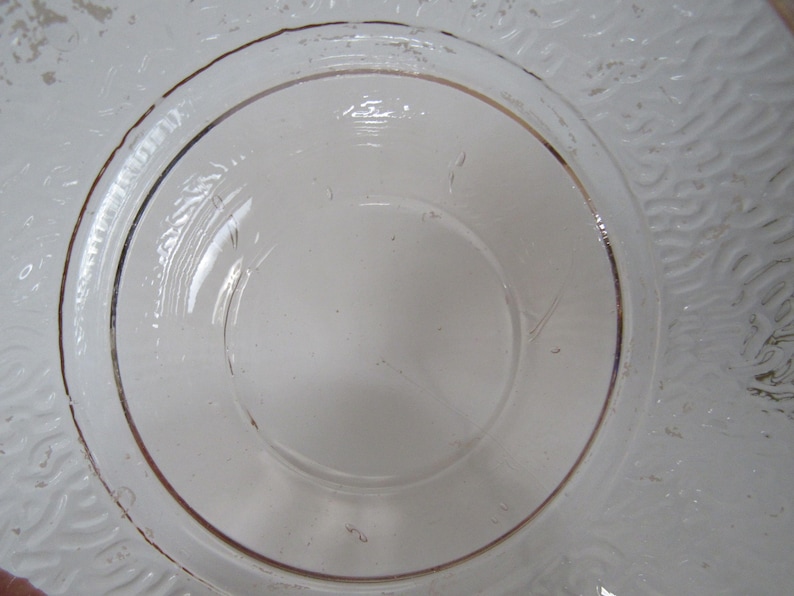May include: Clear glass plate with a raised, circular center and a decorative, textured rim. The rim features a subtle, brown-toned accent. The plate's design is simple and elegant, suitable for serving or display.
