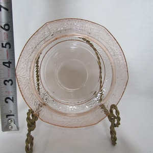 May include: A vintage pink glass saucer with a textured rim and a central depression, displayed on a decorative brass stand. The saucer is approximately 4 inches in diameter. The glass has a delicate, translucent quality.