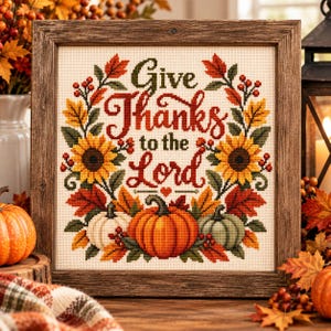 Puede incluir: Una obra de punto de cruz cuadrada en un marco de madera rústica con el texto Give Thanks to the Lord en rojo y verde oscuro. El diseño incluye una corona de girasoles amarillos, calabazas naranjas y verdes, bayas y hojas de otoño.