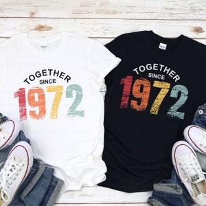 May include: Two t-shirts with a vintage-style design. The white t-shirt has the text "Together Since 1972" in rainbow colors. The black t-shirt has the same text in rainbow colors.