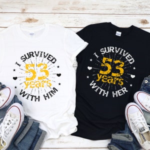 May include: Two t-shirts with a distressed graphic design. The white t-shirt says "I survived 53 years with him" and the black t-shirt says "I survived 53 years with her".