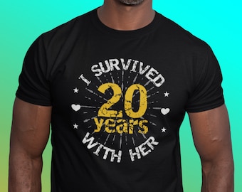 May include: Black t-shirt with a white graphic that says "I survived 20 years with her". The graphic features a large gold number 20 with a starburst design and hearts.