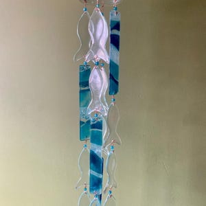 Campana de viento grande con atrapasol y portavelas. Fabricada con vidrio reciclado. Doce peces colgados junto a verdes y azules marinos.