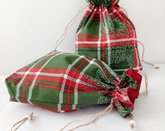 May include: Two green and red plaid drawstring bags with white trim. The bags are made of fabric and have a rustic, farmhouse style.