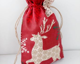 May include: Red fabric gift bag with a white reindeer and snowflake pattern. The bag has a drawstring closure and is made of a soft, textured fabric.