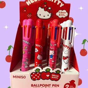 Puede incluir: Una caja expositora que contiene varios bol&iacute;grafos multicolor con gr&aacute;ficos de los personajes Hello Kitty y My Melody. Los bol&iacute;grafos tienen puntas de 0,8 mm y seis colores de tinta. El empaque rojo y blanco incluye ilustraciones de cerezas y texto.