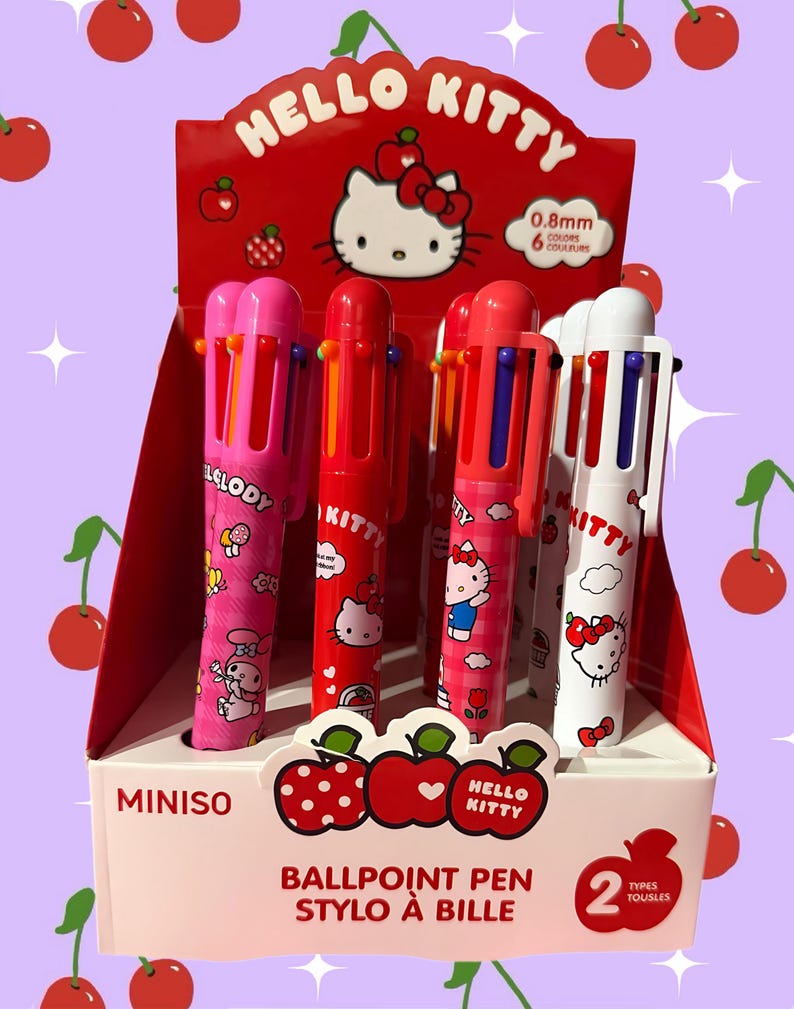 Puede incluir: Una caja expositora que contiene varios bol&iacute;grafos multicolor con gr&aacute;ficos de los personajes Hello Kitty y My Melody. Los bol&iacute;grafos tienen puntas de 0,8 mm y seis colores de tinta. El empaque rojo y blanco incluye ilustraciones de cerezas y texto.
