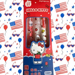 Puede incluir: Una caja de embalaje rectangular roja que contiene tres bol&iacute;grafos de gel con gr&aacute;ficos de Hello Kitty. La caja muestra el texto HELLO KITTY, Joytop y 0.5. El patr&oacute;n de fondo consiste en banderas estadounidenses, globos azules y gafas de coraz&oacute;n.