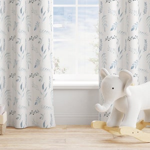 Puede incluir: Cortinas blancas con un patrón repetido de hojas y ramas azules y grises. Un elefante de peluche blanco sobre una base de balancín de madera está frente a una ventana. Una pequeña cesta de mimbre con libros está en el suelo.