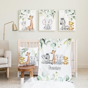 May include: A nursery set with watercolour illustrations of safari animals. The set includes three framed canvas prints, a throw pillow, and a baby blanket. The blanket is personalised with the name "Theodore". The artwork features a giraffe, elephant, zebra, and lion.