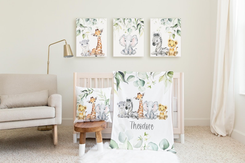 May include: A nursery set with watercolour illustrations of safari animals. The set includes three framed canvas prints, a throw pillow, and a baby blanket. The blanket is personalised with the name "Theodore". The artwork features a giraffe, elephant, zebra, and lion.