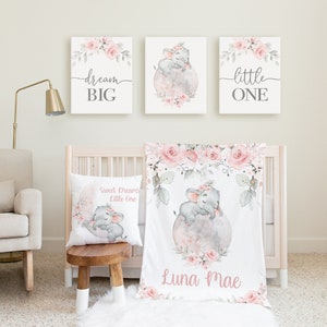 May include: A nursery decor set with a pink and gray color scheme. The set includes a crib blanket, a pillow, and three wall prints. The crib blanket features a watercolor illustration of an elephant with pink flowers and the name "Luna Mae". The pillow features a similar illustration with the text "Sweet Dreams Little One". The wall prints feature the text "dream big", "little one", and a watercolor illustration of an elephant with pink flowers.
