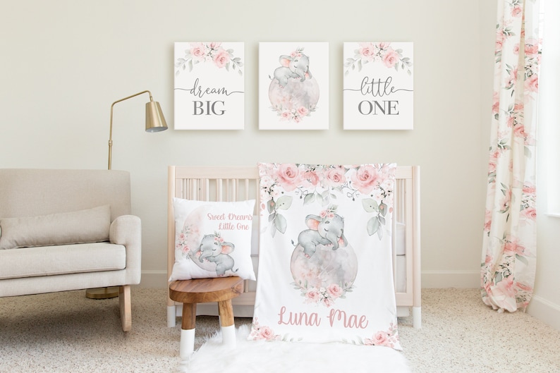 May include: A nursery decor set with a pink and gray color scheme. The set includes a crib blanket, a pillow, and three wall prints. The crib blanket features a watercolor illustration of an elephant with pink flowers and the name "Luna Mae". The pillow features a similar illustration with the text "Sweet Dreams Little One". The wall prints feature the text "dream big", "little one", and a watercolor illustration of an elephant with pink flowers.