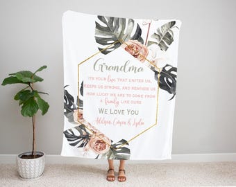 Può includere: Coperta bianca con un design floreale e la parola "Nonna" in oro. La coperta presenta una cornice geometrica dorata con il testo "TI AMIAMO". Il design include fiori e foglie in stile acquerello.
