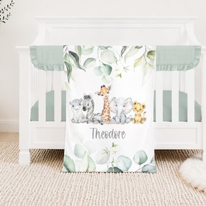 May include: A white cot with a mint green bumper and a matching blanket. The blanket features watercolor illustrations of a zebra, giraffe, elephant, lion, and other animals. The name "Theodore" is printed on the blanket.