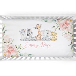 Peut inclure: Un drap de lit blanc pour bébé avec un motif floral rose et un groupe d'animaux de la savane. Le drap porte le nom "Emmy Rose" écrit en lettres roses.