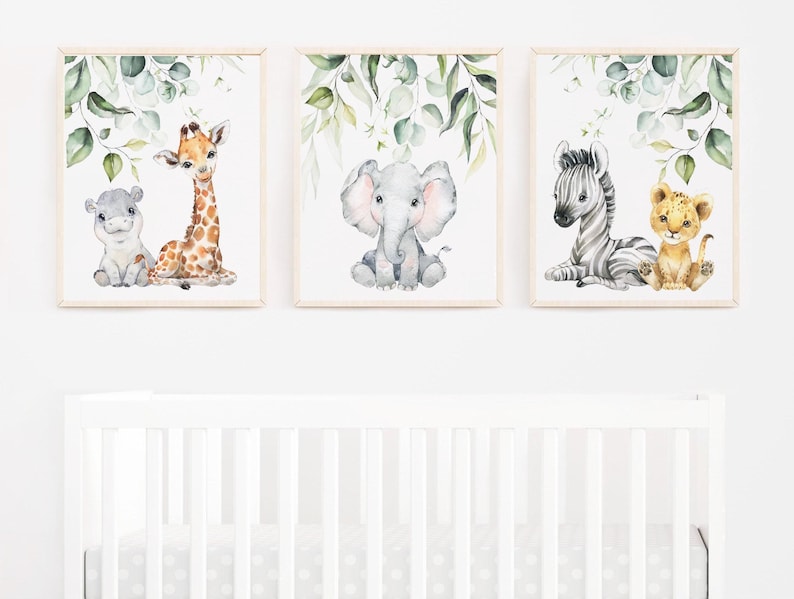 May include: Three framed watercolour prints. Each features a baby animal: a hippo and giraffe, an elephant, and a zebra with a lion cub. Green leaves border each print, set against a white background.