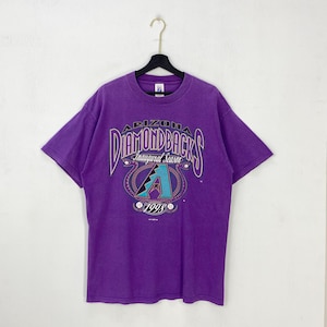 May include: Purple t-shirt featuring the Arizona Diamondbacks logo with the text "Inaugural Season 1998". The graphic includes the team name in a stylized font, a teal "A" and baseballs.