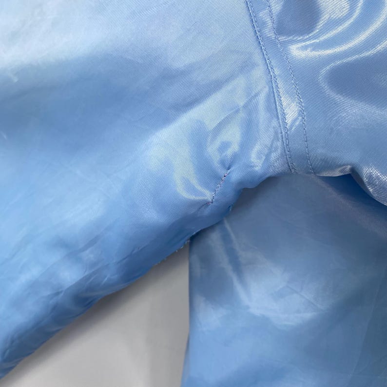 Puede incluir: Primer plano de una tela de sat&eacute;n azul claro, que muestra la textura y las costuras. La tela es suave y brillante, con sutiles variaciones de color. La imagen se centra en los detalles del material.