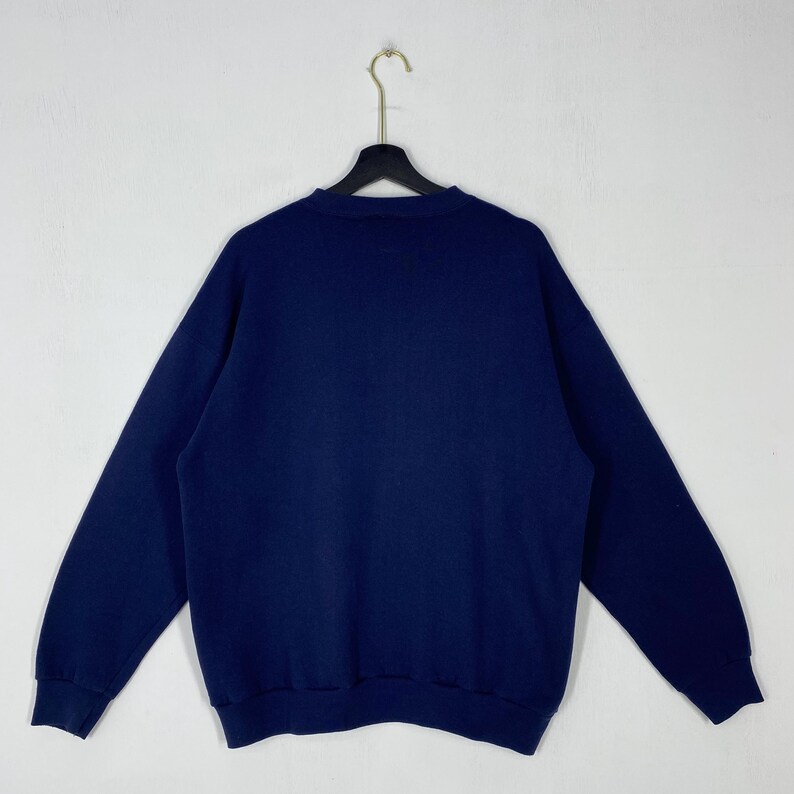 May include: A navy blue sweatshirt with long sleeves, hanging on a black hanger. The sweatshirt is made of a soft material and is displayed against a white background. The garment is clean and appears to be in good condition.