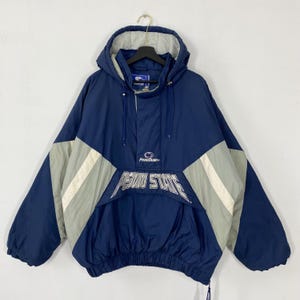 Puede incluir: Chaqueta anorak con capucha azul marino y gris con la inscripción "PENN STATE" en la parte delantera. La chaqueta tiene una capucha con cordón y un bolsillo delantero. La chaqueta es de Starter.