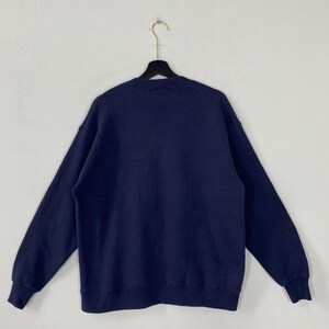 K&ouml;nnte beinhalten: Ein marineblaues Sweatshirt h&auml;ngt an einem schwarzen Kleiderb&uuml;gel. Das Sweatshirt hat einen Rundhalsausschnitt und lange &Auml;rmel mit gerippten B&uuml;ndchen. Das Kleidungsst&uuml;ck ist aus einem weichen, bequemen Material gefertigt.