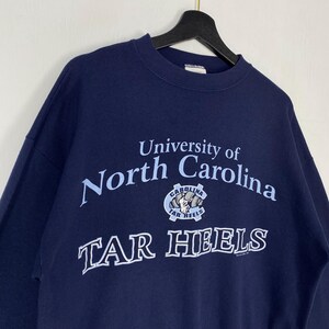 May include: Navy blue sweatshirt with the text "University of North Carolina" in light blue, and a Tar Heels logo. The sweatshirt is suspended from a black hanger.