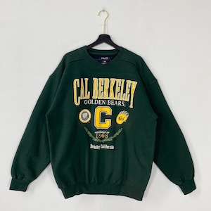 Peut inclure: Sweat-shirt vert foncé avec l'inscription "Cal Berkeley Golden Bears" en lettres jaunes. Comporte un grand "C" jaune et d'autres graphiques. Le texte "established in 1868" et "Berkeley California" est également visible.