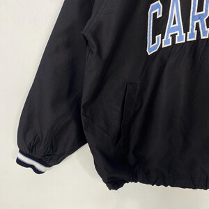 May include: Black jacket with the word "CAR" in light blue and white lettering across the chest. The jacket has a pocket on the front and a striped cuff on the sleeve. The jacket is made of a lightweight material.